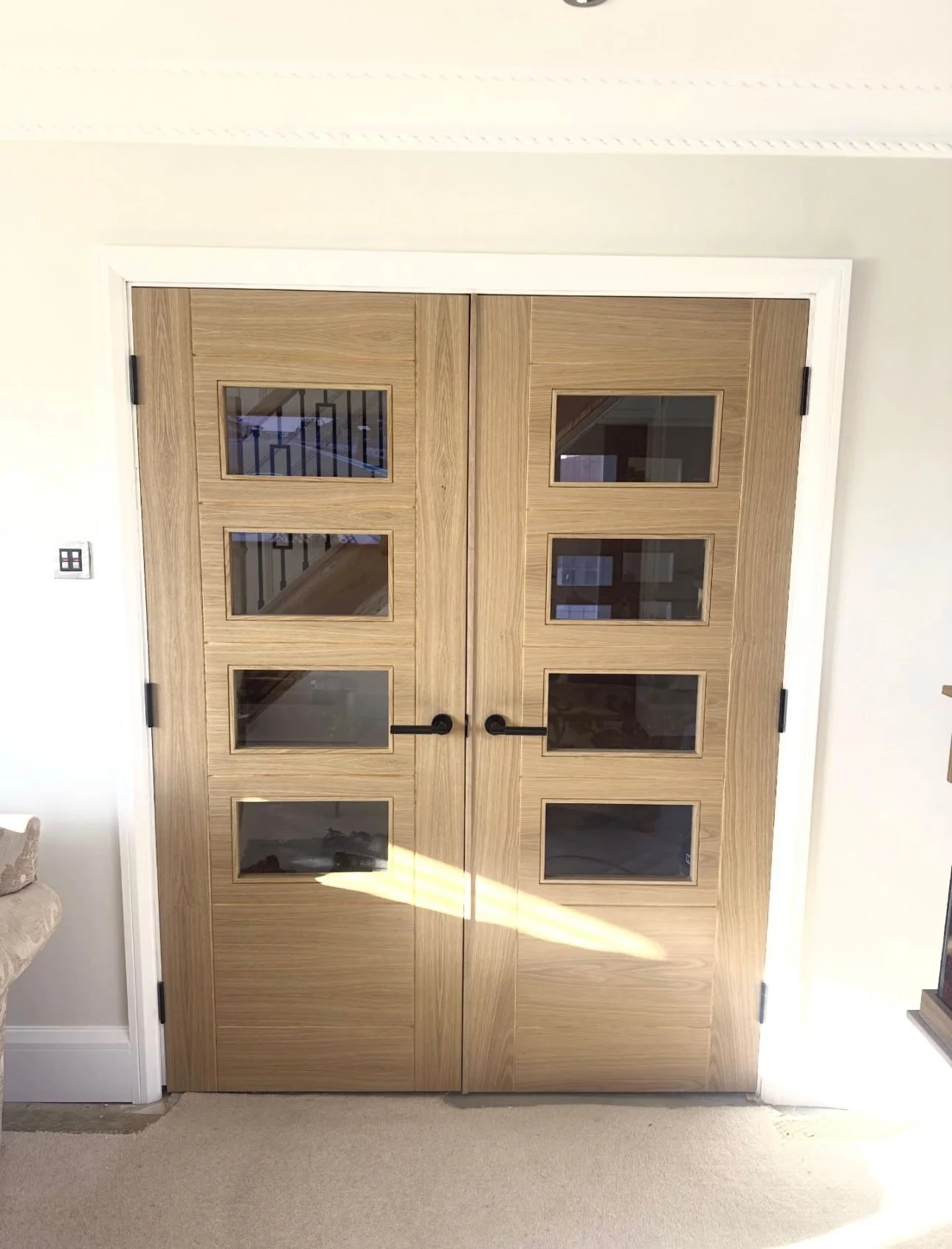Oak double internal doors with four-panel glass inserts and black handles in domestic interior