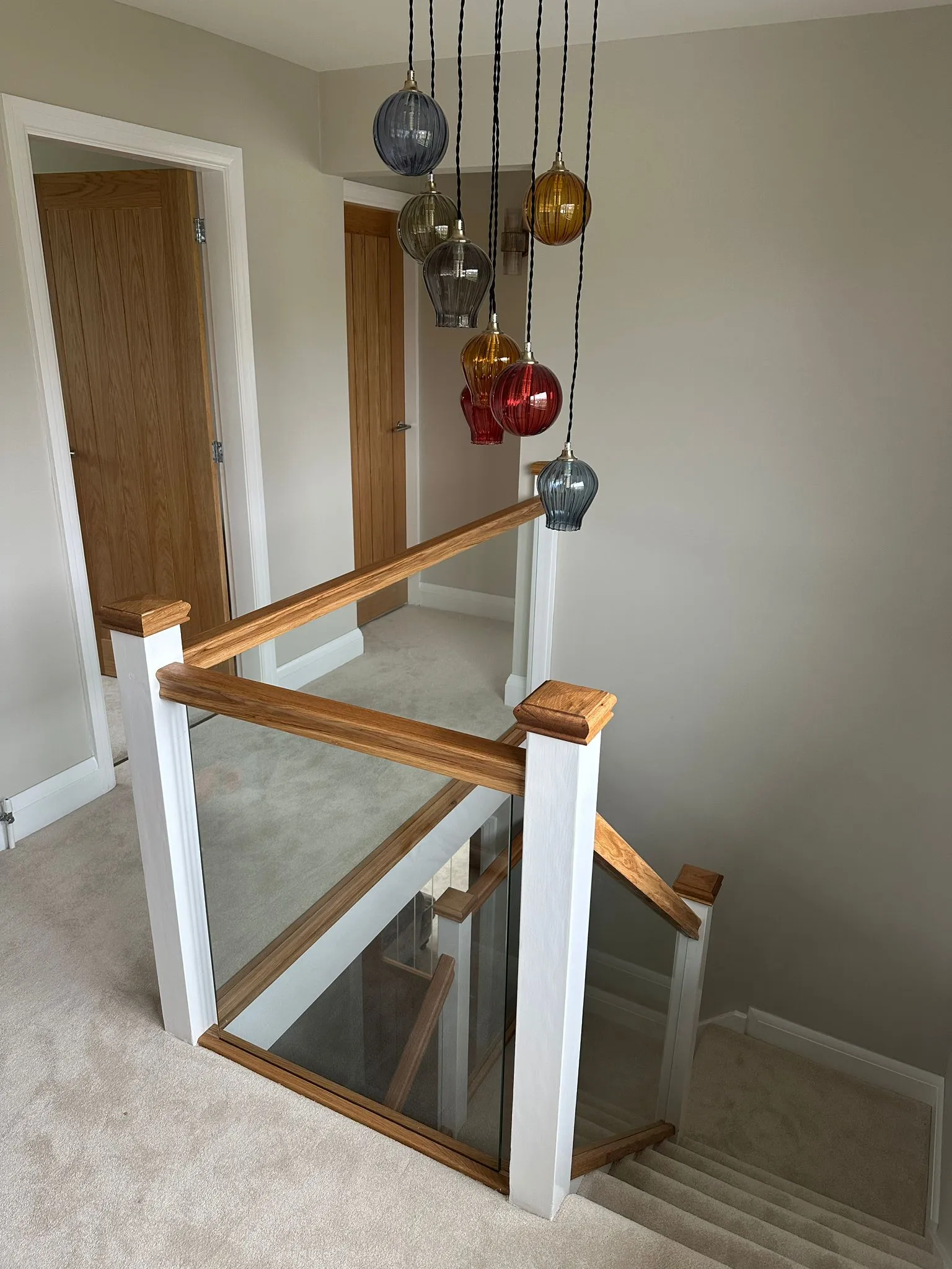 Oak and glass staircase landing with colourful pendant lights